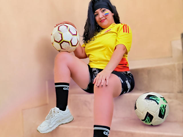 BbwLuxuryMuse com cabelo preto, camisa de futebol amarela, shorts pretos, meias brancas e tênis brancos, segurando bolas de futebol, sentada nas escadas, usando uma faixa de cabelo preta, sorrindo..