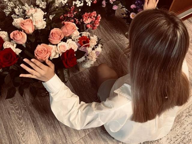 Deana Gramlich, con capelli marrone chiaro, una camicia bianca e il sedere scoperto, è inginocchiata e sta toccando rose rosa e rosse su un pavimento di legno..