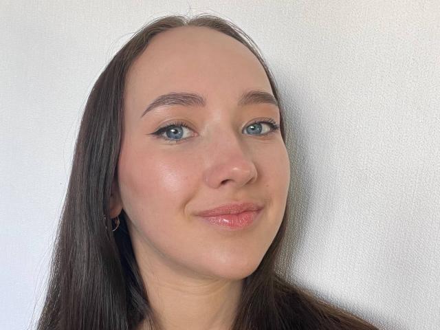 Valorie Santulli ha gli occhi azzurri, labbra rosa lucide e capelli castani lisci, indossa piccoli orecchini a cerchio e ha un leggero sorriso sul suo viso chiaro..