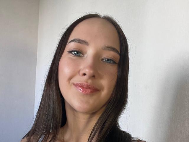 Valorie Santulli hat strahlend blaue Augen, glattes braunes Haar und glänzende rosa Lippen, mit einem leichten Lächeln auf ihrem hellen Gesicht. Ihre Augenbrauen sind ordentlich geformt..