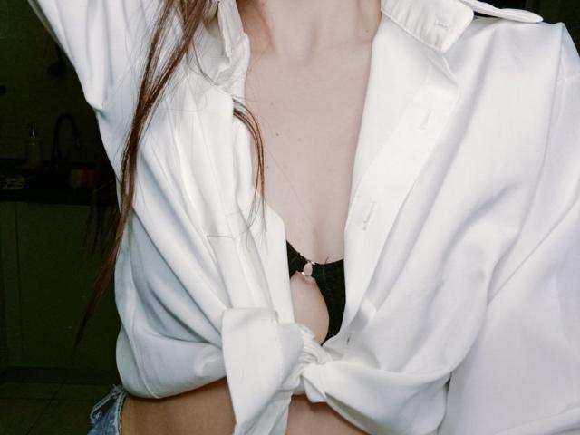 WollyMolly's white shirt is tied below her tits, exposing a black bra with a pink bow. Her brown hair is partially visible.