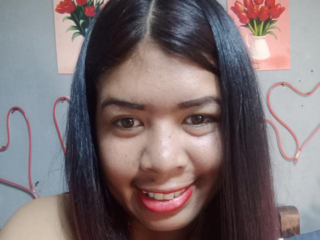 MariahSquirting69 ha i capelli neri e lisci, gli occhi marroni e il rossetto rosso. Sorride con la lingua leggermente fuori, mostrando i denti. Sullo sfondo, c'è una decorazione a forma di cuore rossa..