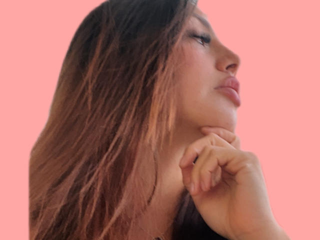 Le labbra piene di GalaMalkova, i suoi capelli castano chiaro ondulati e la mano sotto il mento su uno sfondo rosa. I suoi occhi sono chiusi e il suo naso è leggermente all'insù..