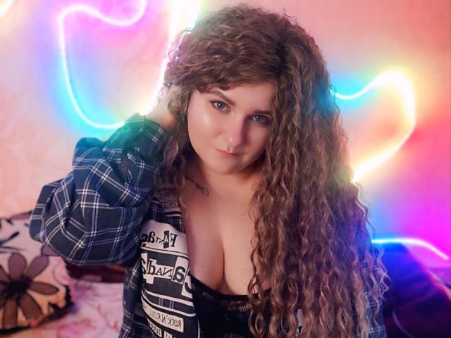 MinistraX with long curly brown hair, wearing a plaid shirt, black top showing big boobs, holding her hair, looking at the camera, neon lights in the background.