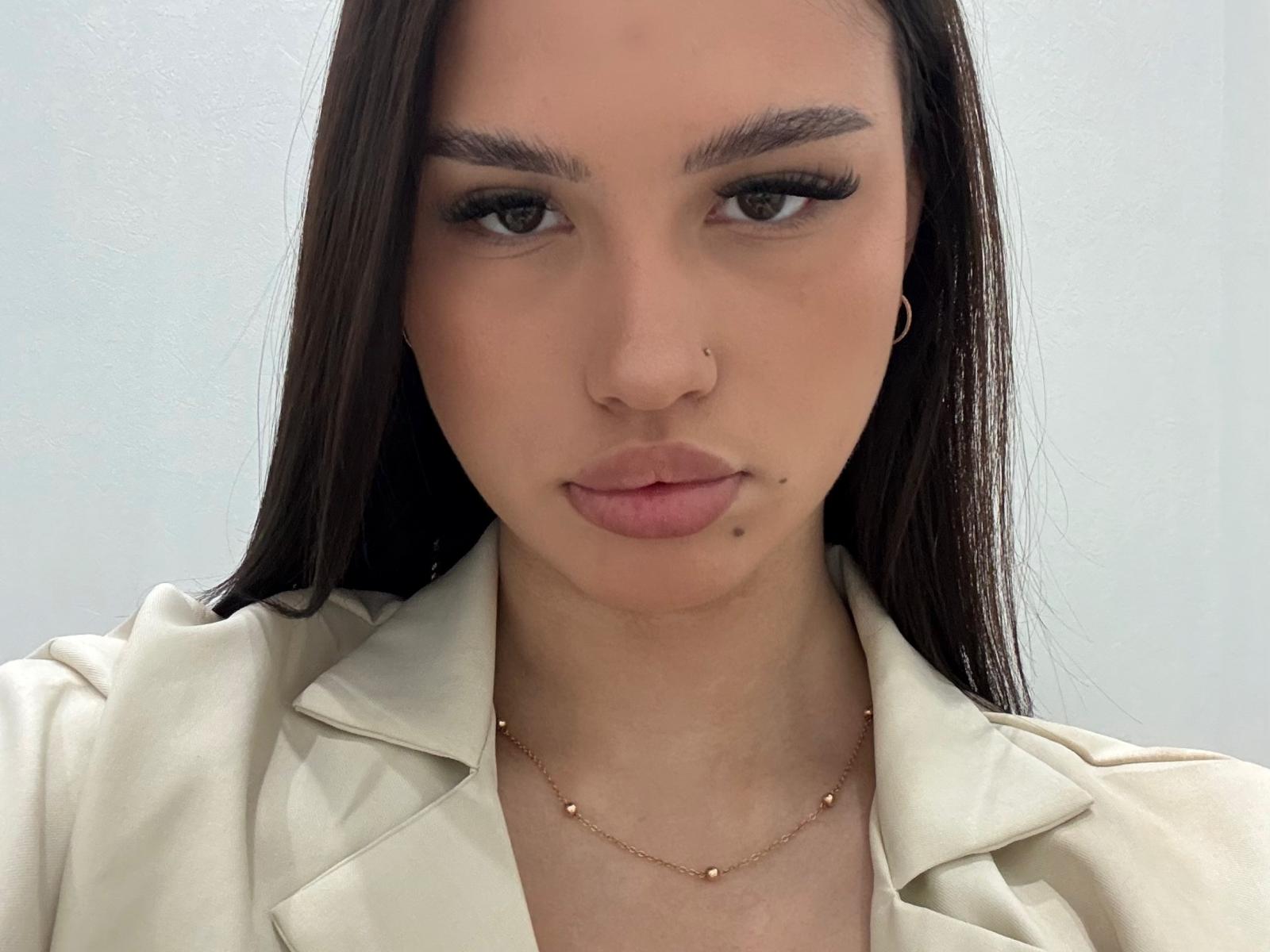 Savanna Hartless, con i suoi lunghi capelli scuri, indossa una giacca bianca, ha un piercing al naso, una lentiggine sul labbro inferiore e una collana d'oro con piccole perle..