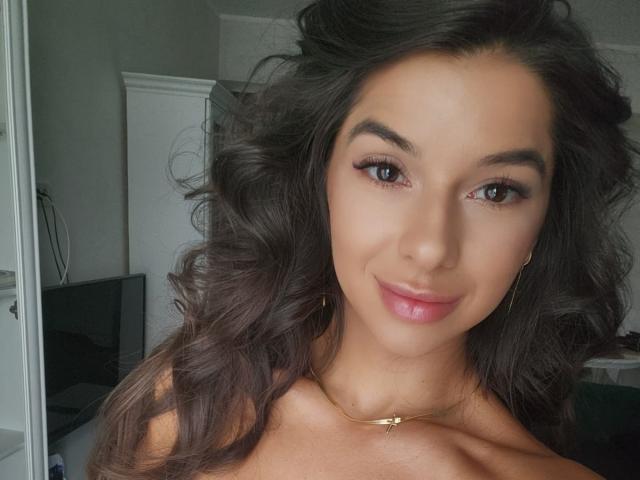 SandyBoobs tem cabelos cacheados castanho-escuros, olhos castanhos e um sorriso adorável. Ela está usando um colar dourado e pequenos brincos, com um batom rosa claro. Seus seios não estão visíveis..