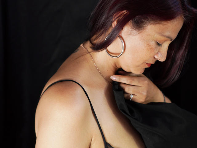 MilenneSexy heeft bruine huid, rood haar en sproeten. Ze trekt een zwarte top uit, waardoor haar blote schouder en bovenborst zichtbaar zijn. Ze draagt een ring en oorringen..