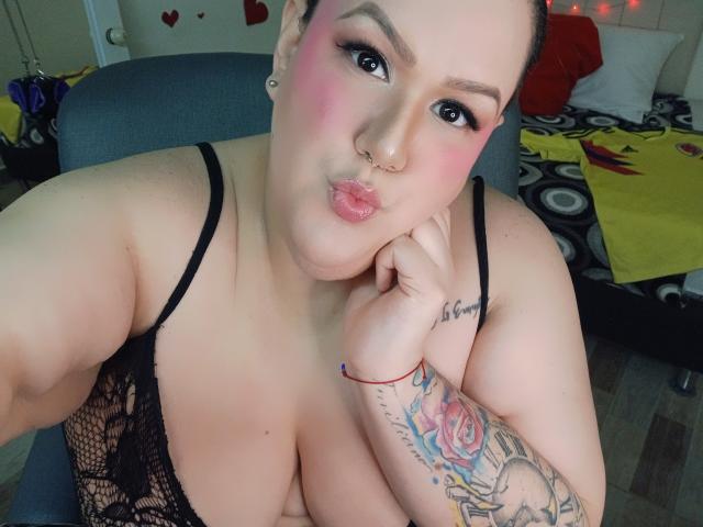 GiiannaMorrys with pink blush, black lace top, pouty lips, nose ring, tattooed arm, and big boobs, taking a selfie, showing off her cleavage and cute face.
