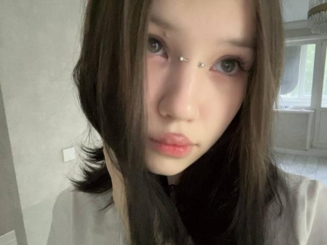 Shaniqua Fairleigh, avec ses cheveux bruns lisses, sa peau claire et un piercing au nez, regarde l'appareil photo avec des lèvres rosées légèrement pincées. Ses yeux sont foncés et légèrement baissés..