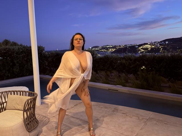 BadAngel è in piedi, vestita con una tunica bianca e trasparente, che mette in mostra un seno abbondante e una vulva piccola e visibile. Si trova all'aperto al crepuscolo, indossando dei tacchi, con uno skyline cittadino sullo sfondo..