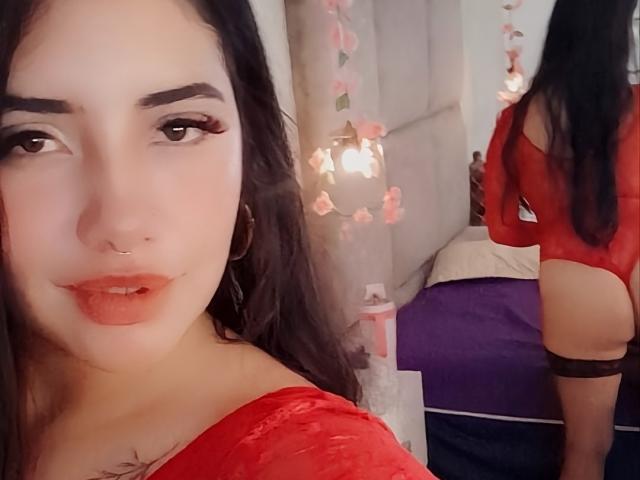 EmaFiore with red lace lingerie, showing her ass in a mirror selfie. She's got long black hair, a nose ring, and red lipstick. Her tits are covered by the lace.