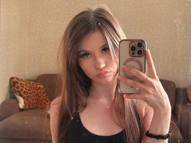 Latisha Streetman, com cabelos castanhos longos, olhos verdes e lábios carnudos, está tirando uma selfie no espelho com um celular, vestindo uma regata preta, mostrando seus seios levemente..
