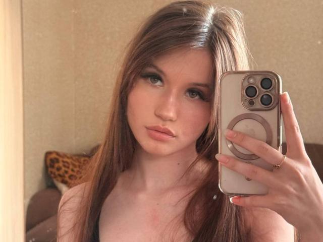 Latisha Streetman, com cabelos castanhos longos, olhos verdes e lábios rosados, segurando um celular com uma capa de anel, vestindo uma blusa preta, tirando uma selfie em um espelho..