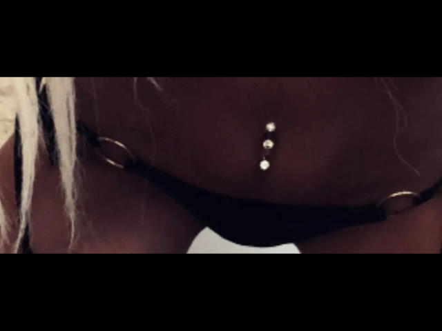 Malialee-hots schwarzer String mit goldenen Ringen, der eine Bauchnabelpiercing mit zwei glänzenden silbernen Kugeln zeigt, in einem dunklen, Detailaufnahme..