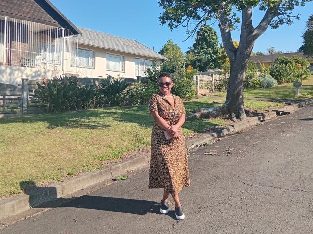 AfusionQueen stands on a sunny street, wearing a brown leopard print dress, black shoes with white soles, and sunglasses, with hands crossed in front of her.