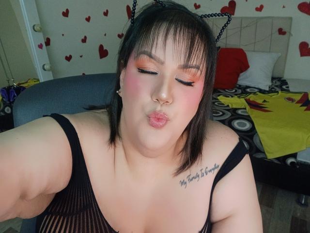 GiiannaMorrys with cat ears, pouty pink lips, orange eyeshadow, black mesh top, tattoo on right shoulder, puffy cheeks, nose ring, and short brown hair, taking a selfie.