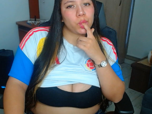 KrisGarner with long brown hair, puffy red lips, and a nose ring, sucking her finger, wearing a white and blue sports shirt, black bra, exposing her tits.
