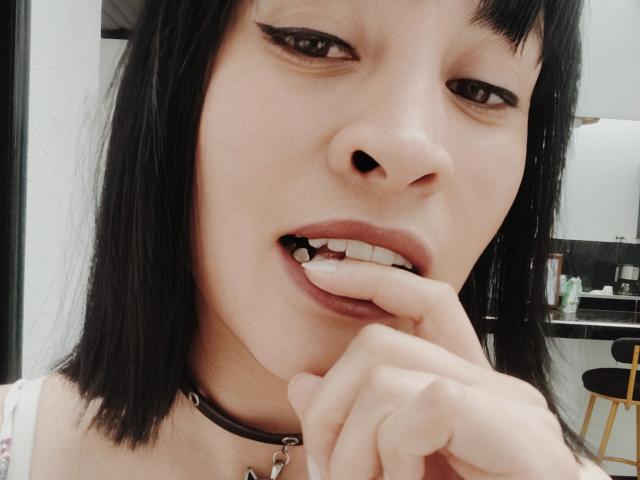 IssisDiosa ha i capelli neri, indossa un choker con un anello metallico, si morde un dito mostrando i denti, e ha l'eyeliner con la forma ad "ala", appare leggermente annoiata..