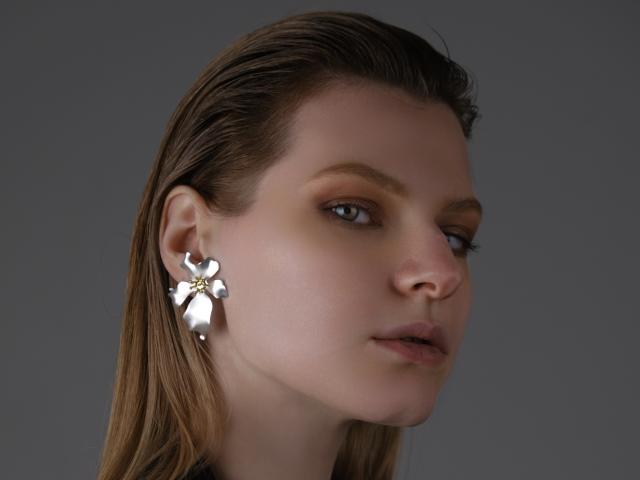 MaryHigginsx, con i capelli castano lucidi, indossa un orecchino a forma di fiore metallico all'orecchio sinistro, ha un'espressione seria, un trucco leggero e una carnagione chiara e uniforme..