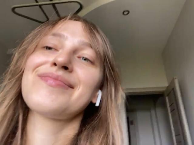 Een Ierse vrouw met blond haar, witte oordopjes en een lichte grijns, met zachte, roze lippen en een lichte huid, in een casual selfie..