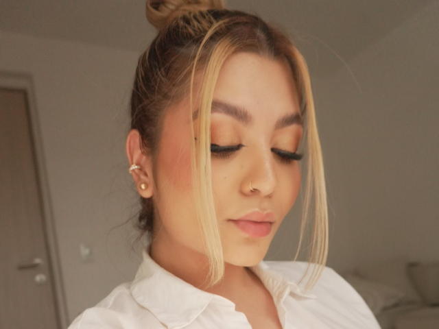 Laumont has blonde hair in a bun, closed eyes with winged eyeliner, pink blush, nose ring, and white shirt. Her tits are not visible. Soft, cute, and sexy.