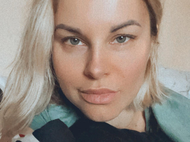 BelleLisaG a les cheveux blonds, les yeux verts, et elle fait la moue avec les lèvres légèrement pincées. Elle porte un haut vert, et son visage est centré dans l'image..