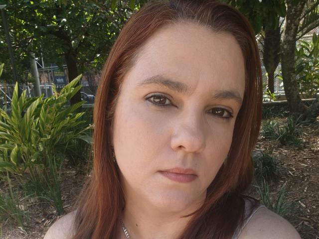 Amelia Wilson tem olhos castanhos, cabelo ruivo e uma expressão neutra. Seu nariz é ligeiramente arrebitado, e ela está usando um colar de prata. Ela está olhando diretamente para a câmera..
