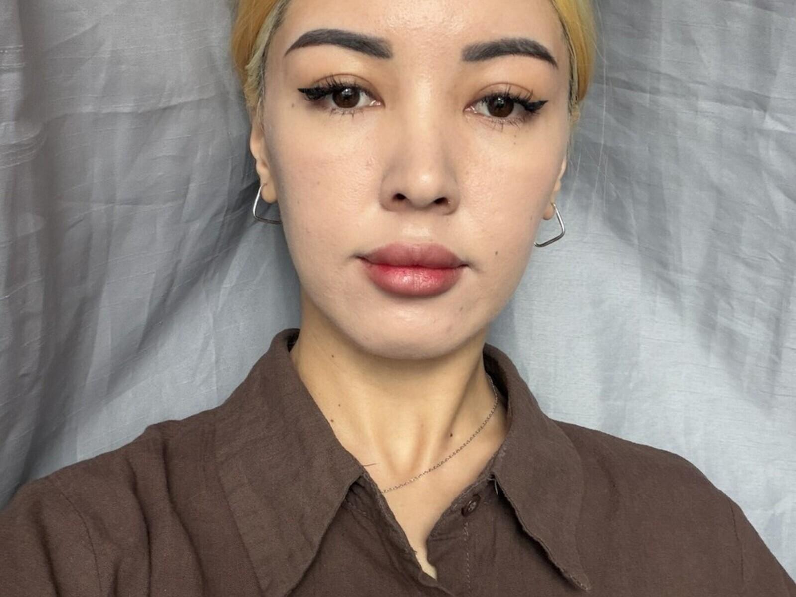 JuliaOverbough heeft een lichte huid, blond haar, dikke wenkbrauwen, lange wimpers, roze lippen, draagt een bruin shirt, kleine oorringen en een delicate ketting..