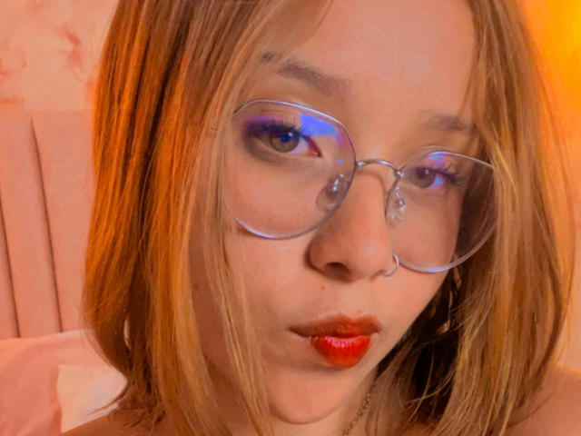 HeraJuno heeft lichtbruin haar, heldere glazen, rode lippenstift en blauwe oogmake-up. Ze kijkt naar beneden met een lichte frons. Ze heeft een kleine zilveren ring in haar neus..