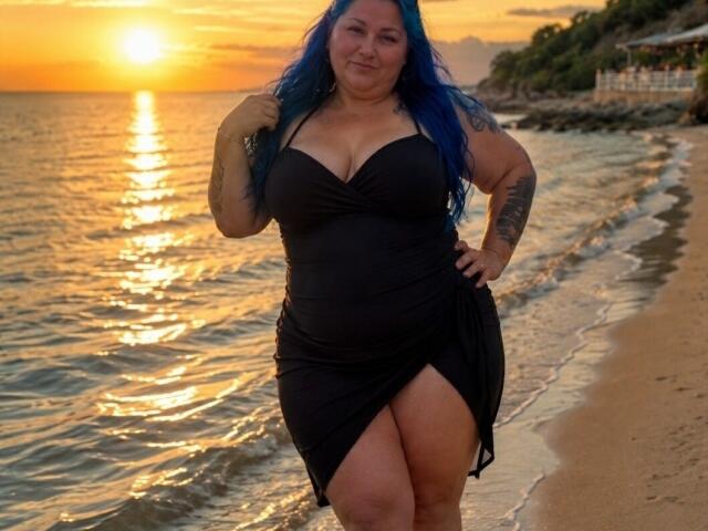 BlondyBigBoobs con cabello azul, vestida con un vestido negro, de pie en una playa al atardecer, mostrando su gran trasero y pechos, con una mano en la cadera, tatuaje en el brazo, sonriendo..