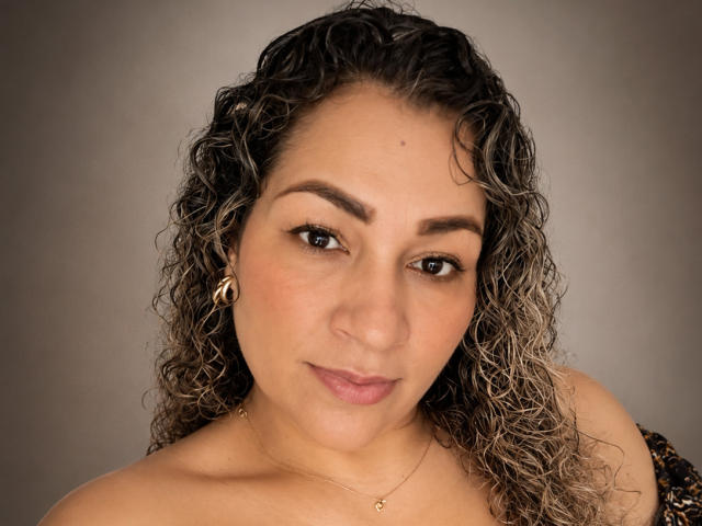 Samanttha Smith tiene el cabello castaño rizado, ojos marrones y una ligera sonrisa. Lleva un arete de aro dorado y un collar delicado con un pequeño dije..