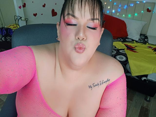 GiiannaMorrys with pink eyeshadow, puffy lips, and a pink mesh top, showing off her big boobs and tattoo reading "My future is foggy." She's pouting.