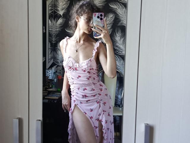 AlyceErway with curly hair, wearing a pink floral dress with a high slit, showing her thigh and a hint of her pussy. She's taking a mirror selfie.