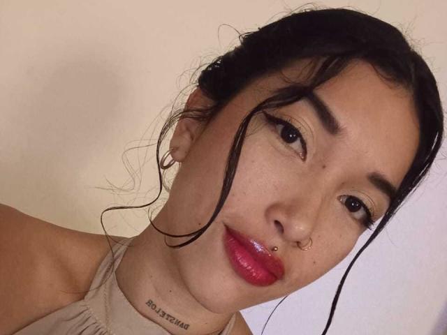 Krystal Evans tem cabelos escuros e desalinhados, um piercing no nariz, lábios vermelhos e brilhantes e uma tatuagem abaixo do queixo. Seus olhos castanhos estão semicerrados, e ela está vestindo uma blusa bege..