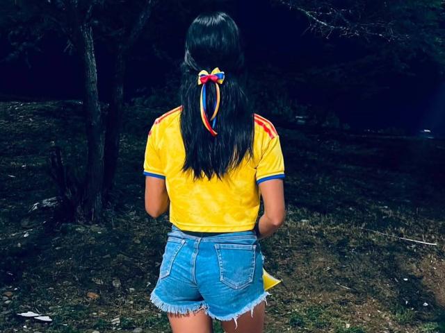 LaBandy, avec de longs cheveux noirs attachés dans un ruban coloré, portant une chemise jaune tie-dye et un short en jean usé, se tient debout, le dos à la caméra..