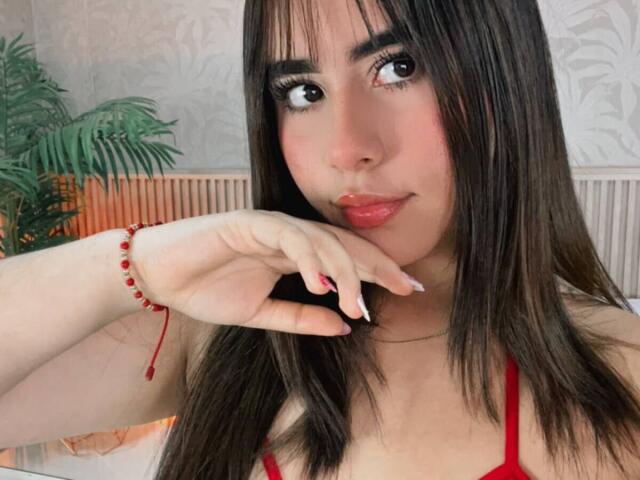 OliviaSanda has long dark hair, pink lipstick, and is touching her lips with red-manicured fingers. She wears a red bra and a red bead bracelet.