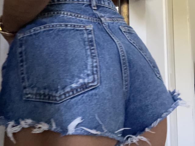 SandraSweet's ass in a blue, frayed denim skirt with visible pockets and white thread at the bottom. Her skin is light brown, and she's wearing a bracelet.