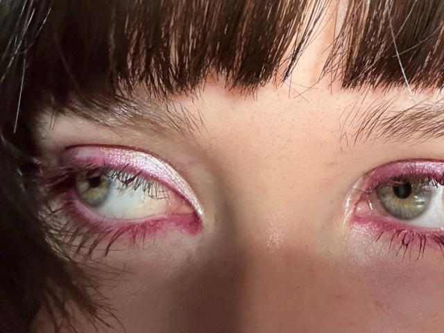 Os olhos de JaclynPalczewski são de um verde escuro, com maquiagem cintilante rosa-clara nas pálpebras e delineador rosa. Suas sobrancelhas castanhas e o cabelo castanho-escuro aparecem na parte superior da imagem..