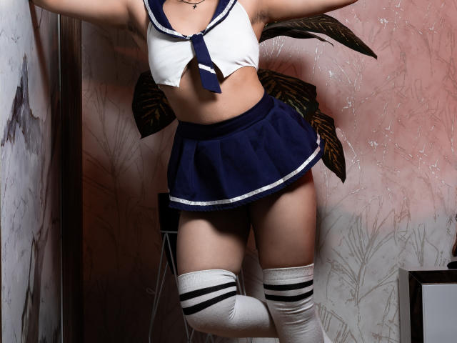 DaryMoon in a sailor-style outfit with a white crop top, navy blue skirt, white thigh-high socks with black stripes, and no visible pants, showing her pussy.
