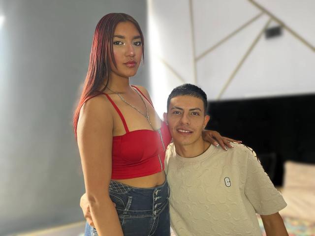 CelesteAndBlake, con lunghi capelli rossi, un top rosso che mostra il seno e jeans blu, è in piedi accanto a Blake, con capelli neri corti, una camicia beige e un sorriso carino..
