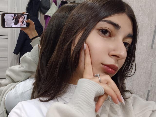 OnieAndreatta, con i capelli castano scuro, indossa una maglietta bianca, si tiene il viso con le unghie curate, sta scattando un selfie con il telefono che mostra il suo viso, ha un anello al dito..