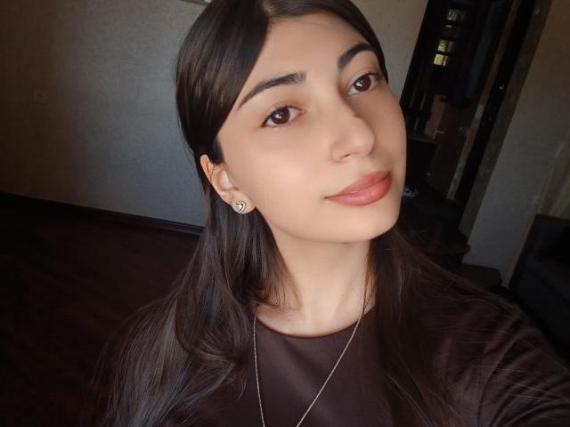 OnieAndreatta, con lunghi capelli castani, occhi marroni e labbra rosate, indossa una maglia marrone, ha un piccolo piercing all'orecchio e una collana d'argento, e sorride dolcemente..