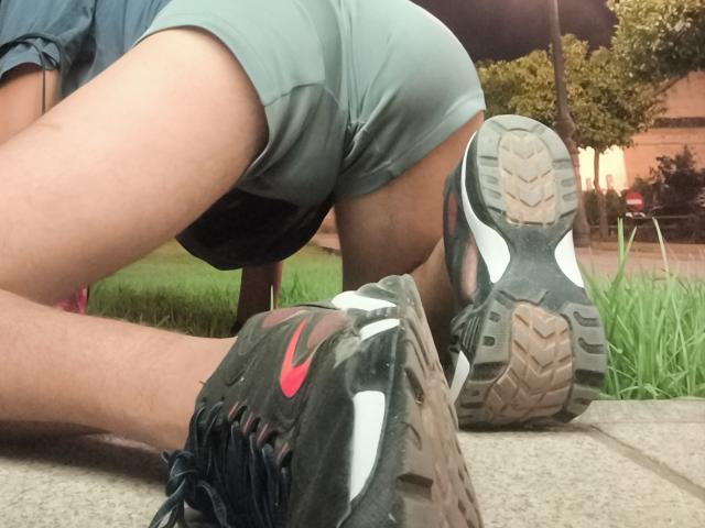 Teronn zit met zijn rug naar de camera, hij draagt groene korte broek en staat op handen en voeten, met Nike sneakers en vuile zolen op een betonnen oppervlak. Op de achtergrond is gras te zien, het is daglicht..