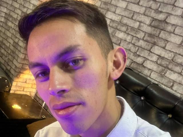 AnderCooper hat kurze, braune Haare, einen hellen Hautton und trägt ein weißes Hemd. Sein Gesicht ist mit violetten und gelben Lichtern beleuchtet. Seine Augen sind leicht gesenkt..