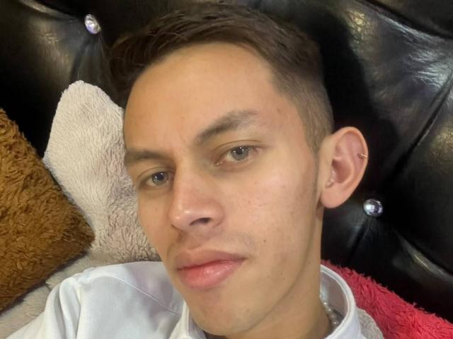 AnderCooper hat kurze, braune Haare, helle Haut und eine kleine Nase. Er trägt ein weißes Hemd, hat ein leichtes Lächeln und ein kleines Ohrring in seinem linken Ohr..