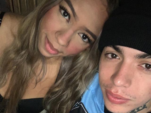 NickySixNine met lang blond haar en make-up, lachend, en NickySixNine met een zwarte muts, beiden met hun gezicht zichtbaar, gekleed in blauwe en zwarte kleding..