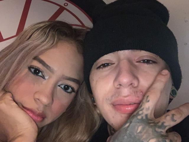 NickySixNine com cabelo loiro e maquiagem, e NickySixNine com um gorro preto, tatuagens e piercings no nariz, fazendo um sinal de "paz". Ambos têm expressões de lábios franzidos e cabeças próximas..