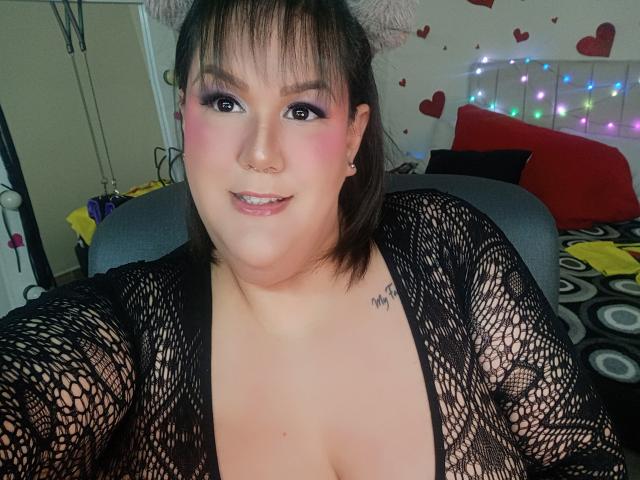 GiiannaMorrys with pink eyeshadow, nose ring, and black fishnet top, showing her big boobs, smiling, has a tattoo on her right shoulder, wearing cat ears.