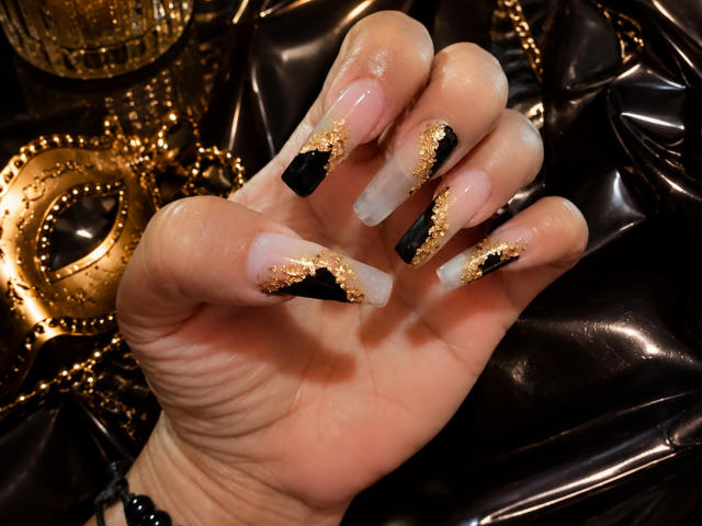 ViancaCastellanos' hand with long, glossy nails, black and gold glitter, and white tips, showing off her sexy, well-manicured boomerangs. Glittery gold and black background.