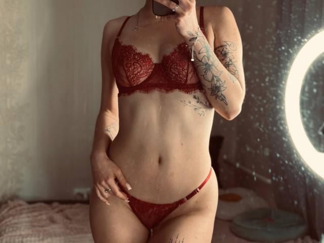 DarceyHeindl in red lace lingerie, showing her tits and pussy, tattoos on arm and side, holding phone, ring on finger, ring light on right.